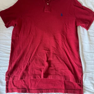 Ralp Lauren Piké - Mörkröd Polo Ralp Lauren Piké tröja i Custom Fit, dvs att den är lite längre baktill. Storlek L och den är använd men går fortfarande att använda. Av sista bilden framgår det litet slitage vid slitsen men är inte jätte synligt när man har på sig det.