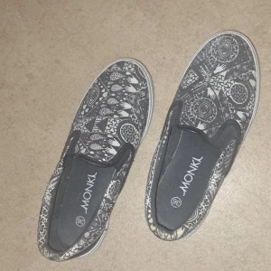 Mönstrade slip-on skor från Monki - Säljer ett par coola slip-on skor från Monki med ett unikt svartvitt mönster. Skorna är i bra skick och perfekta för en avslappnad stil. De har en bekväm passform och är lätta att ta på och av.