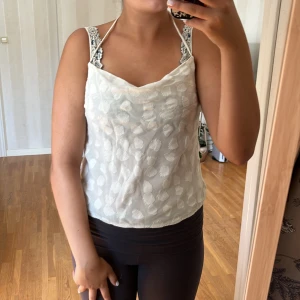 Vit blommig linnetopp från H&M - Säljer en söt vit linnetopp från H&M i storlek XS. Toppen har ett blommigt mönster och smala axelband. Den är perfekt för sommaren och har en knytning i ryggen för en justerbar passform. Toppen är i nyskick.