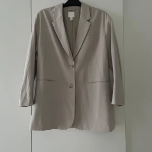 Beige kavaj - Säljer en stilren oversized beige kavaj i storlek xs men passar mer en xs/s. Kavajen har en klassisk design med två knappar framtill och två fickor. Den är långärmad och passar perfekt för både vardag och fest. Materialet känns mjukt och bekvämt. 