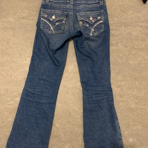 Blå jeans med broderade detaljer - Snygga blå jeans med broderade detaljer på bakfickorna. De har en klassisk femficksdesign och en knappgylf. Perfekta för en avslappnad stil med en touch av unik design. De är low Jens 