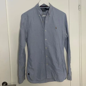 Ralph lauren skjorta - Snygg blå skjorta från Polo Ralph Lauren i slim fit. Skjortan har långa ärmar och knappar framtill samt en broderad logotyp på bröstet. Perfekt för en stilren look.