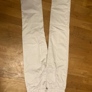 Beige chinos jeans från Lager 157  - Snygga vita chinos med en klassisk design. De har en rak passform och är perfekta för en stilren look. Byxorna har knappar och dragkedja framtill samt hällor för bälte.