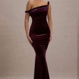 Vinröd axelbandslös långklänning - Elegant vinröd långklänning i sammet med offshoulder-design. Klänningen har en figurnära passform som framhäver silhuetten och ger en lyxig känsla. Perfekt för speciella tillfällen.
