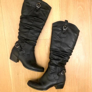 Svarta boots - Snygga svarta stövlar i skinn med dekorativa spännen och låg klack. Perfekta för en stilren look.
