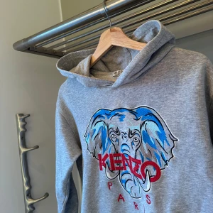 Grå fräsch hoodie från Kenzo - Säljer en snygg grå hoodie från Kenzo. Perfekt för en avslappnad stil med en touch av färg. Hoodien har en klassisk passform och är tillverkad i mjukt material. Ny pris: 1449kr