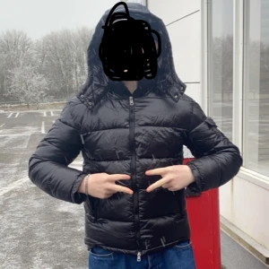 Svart dunjacka från Moncler - Säljer en snygg svart dunjacka från Moncler med huva och dragkedja. Jackan har en quiltad design och Moncler-logga på ärmen. Perfekt för kyliga dagar och håller dig varm och stilren. 🖤