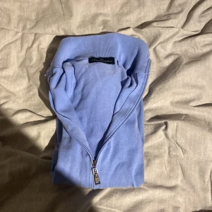 Blå helzip  - Säljer en ljusblå helzip från New Sensation med dragkedja framtill. Tröjan har långa ärmar och ribbade muddar vid ärmslut och nederkant. Perfekt för en avslappnad stil.