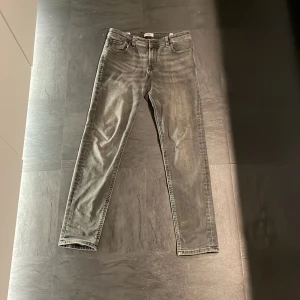 Grå jeans från Jack & Jones - Snygga grå jeans från Jack & Jones med en klassisk femficksdesign. De har en knapp och dragkedja framtill och är perfekta för en avslappnad stil. Passformen är slim och de är tillverkade i ett bekvämt denimtyg. Köpt på Jack & Jones.