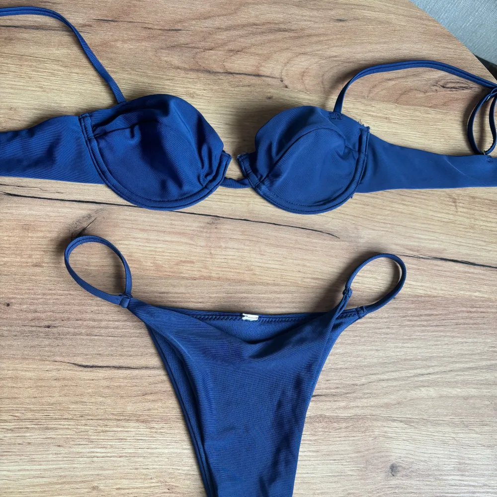 Snygg mörkblå bikini med bygel-bh och justerbara axelband. Trosorna har en klassisk design med smala sidor. Perfekt för en dag på stranden eller vid poolen. Alla lappar är bortklippta men bikinin är oanvänd.. Muu.