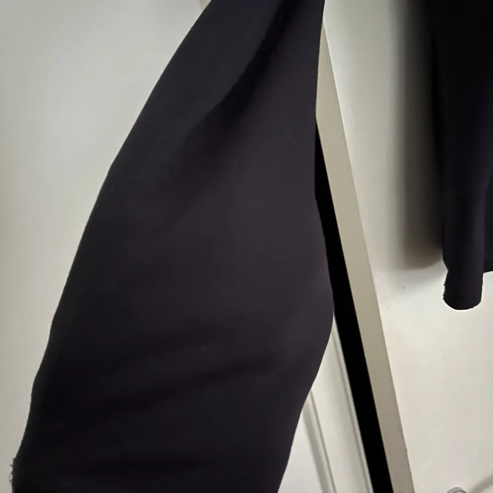 Snygg svart långärmad tröja, softcheln, från Peak Performance med en ljusblå detalj på ärmen. Perfekt för en sportig look. Tröjan har en dragkedja vid halsen och är tillverkad i ett syntetmaterial som ger en skön passform. . Neuletakit & Villapaidat.