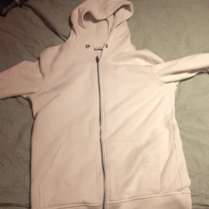 Vit hoodie med zip.  - Säljer en stilren vit hoodie med dragkedja och huva. Perfekt för en avslappnad look. Den har långa ärmar och praktiska fickor framtill. Passar bra till både jeans och mjukisbyxor.