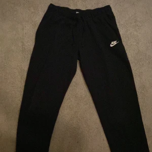Svarta mjukisbyxor från Nike - Säljer ett par svarta mjukisbyxor från Nike med elastisk midja och det klassiska Nike-logotypen på benet. Perfekta för en avslappnad stil eller träning. Tillverkade i mjukt material för extra komfort.