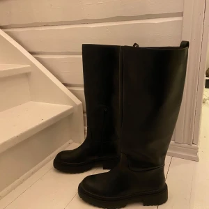 Svarta höga stövlar med dragkedja - Snygga svarta stövlar i skinn med dragkedja på sidan. Perfekta för höst och vinter med en robust sula för extra grepp. Stilrena och enkla att matcha med olika outfits. Helt oanvända!