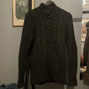 Grå kabelstickad stickad kofta med knappar - Säljer en snygg grå stickad kofta från Duluth Trading Co. med knappar framtill. Koftan är kabelstickad och är tillverkad i en ullblandning med kashmir för extra mjukhet. Perfekt för både stil och komfort. Vintage Stolek S skick 9/10.