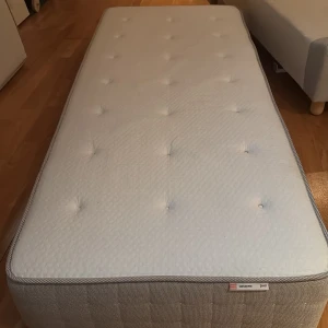 Madrass Hesseng från IKEA - Säljer en bekväm madrass från IKEA, modell Hesseng. Madrassen har en vit ovansida med knappar och en beige kant. Perfekt för en god natts sömn. Levererar ej ni får hämta sängen