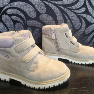 Grå boots från Fila med kardborreband och dragkedja - Säljer ett par grå boots från Fila med praktisk dragkedja och kardborreband för enkel på- och avtagning. Skorna har en robust sula med bra grepp och är perfekta för kyligare väder. Fodrade för extra värme och komfort.