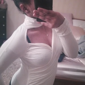 Vit långärmad topp - Säljer en stilren vit långärmad topp med en unik omlott-design och hög krage. Toppen har en tight passform som framhäver figuren. Perfekt för att skapa en elegant look.