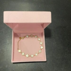 Guldarmband med fyrklöverdesign - Elegant guldarmband med fyrklöverformade länkar. Ena armbandet har vita detaljer medan det andra är glittrigt. Perfekt för att lägga till en touch av lyx till din stil. Samt vattentåligt