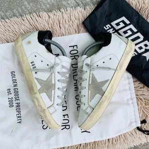 Vita sneakers från Golden Goose - Snygga vita sneakers från Golden Goose med den ikoniska stjärndetaljen i grått på sidan. Skorna har en vintage-look med smutsiga detaljer och svarta hälpartier. Perfekta för en avslappnad stil.