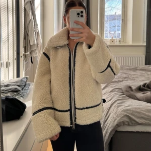 Beige teddyjacka från Zara - Säljer en supermysig beige teddyjacka från Zara med svarta detaljer. Jackan har en dragkedja framtill och en hög krage som håller dig varm. Perfekt för kyliga dagar! 🧥✨