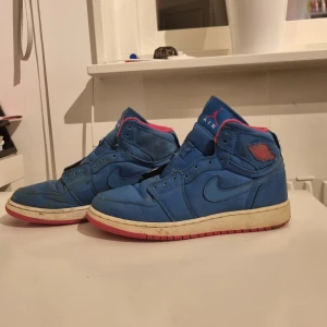 Blå/rosa Nike Air Jordans (fake) - Säljer ett (fake) par blå Nike Air Jordans med rosa detaljer. Skorna har en hög design och en vit sula med rosa undersida. Väl använda men finns många användningar kvar av de, de går o tvätta till lite också så de blir finare