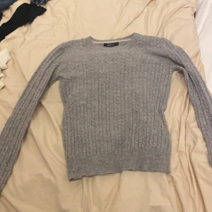 Grå stickad tröja från Gina Tricot - Säljer en stilren grå stickad tröja från Gina Tricot. Tröjan har ett klassiskt kabelstickat mönster och långa ärmar. Perfekt för kyligare dagar.