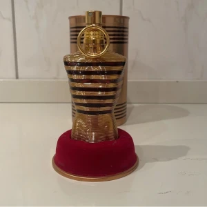 Jean Paul Gaultier Le Male Elixir Parfym - Säljer en elegant parfymflaska formad som en manlig torso i guld och svart från Jean Paul Gaultier. Flaskan har en unik design med horisontella ränder och kommer i en matchande metallcylinder. Perfekt för den som vill ha en lyxig doftupplevelse. Det finns 60-65 ml kvar i flaskan priset kan diskuteras, skriv vid några funderingar 🌟🙌