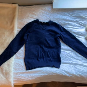 Mörkblå tröja från J.Lindeberg - Säljer en stilren mörkblå tröja från J.Lindeberg med v-ringning. Tröjan har ett diskret broderat märke på bröstet och är perfekt för en klassisk look. Passar bra till både jeans och chinos. Priset går att förhandla!