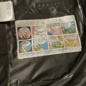 Svart dunväst från Moncler - Säljer en stilren svart dunväst från Moncler. Västen har en klassisk design med en quiltad yta och dragkedja framtill. Perfekt för att hålla värmen under kyliga dagar. Moncler-loggan är diskret placerad på insidan.