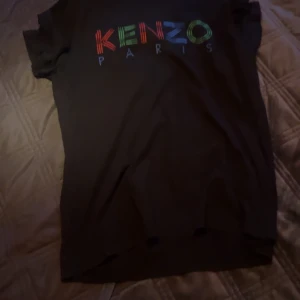 Svart t-shirt från Kenzo - Snygg svart t-shirt från Kenzo med färgglatt tryck av märkesnamnet på framsidan. Perfekt för en stilren och modern look. T-shirten har korta ärmar och är tillverkad i ett mjukt material.