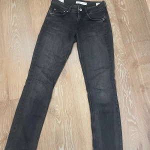 Svarta jeans från Pepe jeans - Snygga svarta jeans från Pepe jeans med en klassisk femficksdesign. De har en knapp och dragkedja framtill och är perfekta för en stilren look. De är lågmidjade och straight. De har inte riktigt en jeans-känsla utan är lite mjukare. De är mörkgrå med lite ljusare partier på låren.
