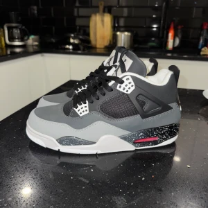 Jordan 4 - Snygga grå och svarta sneakers med vit sula och svarta detaljer. Skorna har snörning och en specklad mellansula med rosa inslag. Perfekta för en stilren look.