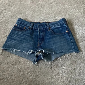 Blå jeansshorts från Levi's - Säljer ett par snygga blå jeansshorts från Levi's med fransiga kanter och klassisk femficksdesign. Perfekta för en avslappnad stil. De har en knappgylf och är lågmidjade för en cool look. Passar perfekt till sommardagar!☀️⛱️🍉Står inte exakt storlek men passar både S och M