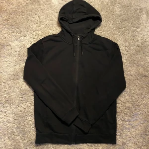 Svart cardigan  - Säljer en stilren svart cardigan. Perfekt för en avslappnad look. Den har långa ärmar och ribbade muddar vid ärmslut och nederkant.