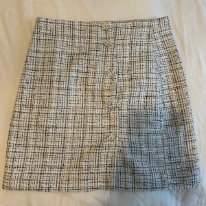 Rutig kjol från H&M - Snygg rutig kjol från H&M i svart och vit. Kjolen har en klassisk A-linjeform och är perfekt för en stilren look. Den är kort och har knappar.  