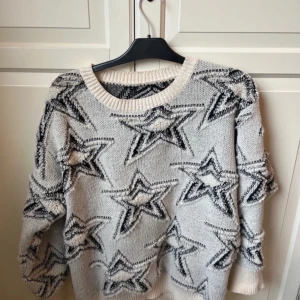 Stickad tröja med stjärnmönster - Säljer en mysig stickad tröja med svart stjärnmönster. Tröjan har långa ärmar och en rund halsringning. Finns ingen lapp så vet ej märket.