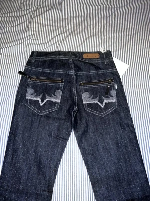 Jeans - Här är en lågmidajade jeans Själva materialet är lite glittrig som ni ser och den har väldigt fina detraljer på fickorna. Jag är 170 och har i storlek S. Byxorna är väldigt små för mig och längs ner de är tajta för mig.  Obs! Kunden står för frakten. 