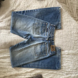 Lågmidjade jeans - Uppskattad low-waist jeans i ljusblå färg och detaljer på fickorna. En av bälteshållarna har åkt bort bak, se bild 3. Mått: Waist - ca 34cm rakt över och hyfsat stretchigt material, innerben - 75cm ( går ej att få fitpic då plagget är för litet) BRA skick