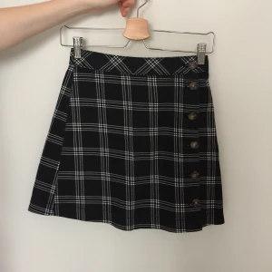 High waisted rutig kjol - Högmidjad kort rutig kjol med knappar på sidan. Köparen står för fraktkostnaden om varan skickas på post.