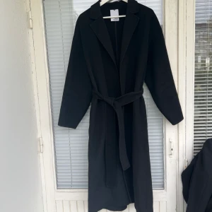 Kappa  - Svart kappa i fint skick säljes! 52% ull, väldigt varm och gosig. Ullbälte medföljer. Inga skavanker eller dylikt. Strl: M, upplevs dock som en onesize beroende på hur man vill att den ska sitta. 