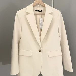 Kavaj/ Blazer - Kavaj/ Blazer, enkelknäppt från Ginatricot i storlek 34. Rak i modellen. Aldrig använd med prislappen kvar! Köpt för 749kr. Extra knappar finns till. Gräddvit i färgen och långa armar.