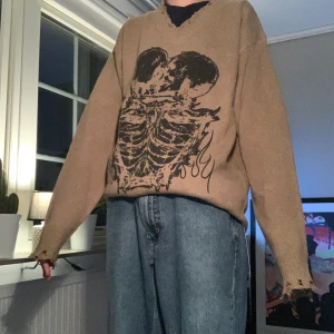 Stickad tröja med skelett tryck. Storlek M - Brun/beige stickad tröja med ett svart skeltt tryck. V-ringad med slitna kanter. Sprillans ny och aldrig använd. 