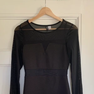 Kort Svart Klänning - Klänning från H&M i storlek 34. Armarna och en del av magen är i mesh och det andra i vanligt tyg. Långarmad och går till låren. Aldrig använd. 115kr + frakt ( cirka 50kr)