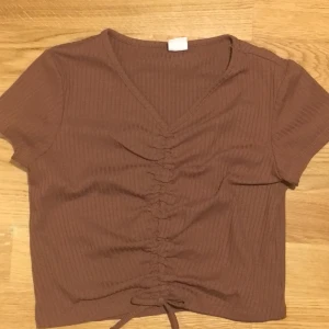 Brun topp med rosett  - Säljer en brun topp från Lindex ( original pris:180) säljer den för att jag bara har använt den 1 gång och inte passar super bra i den. Men skriv till mig om du är intresserad av att köpa😙💗