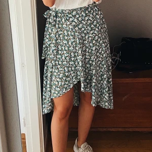 Blommig omlottkjol, strl XS - Härlig, somrig omlottkjol från Lindex med knappar och band i sidan. På bilden har jag vikt upp kjolen lite så den blir kortare, men den kan även bäras lite längre.   Storlek XS  Använd 2 gånger så den är som ny. 