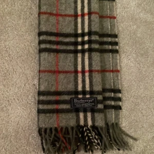Burberry halsduk - Säljer min burberry halsduk som jag fick i julklapp för 2 år sen! Den är grå med röda, vita och svarta ränder på kan också byta mot saker! Skick 7/10 det finns några små hål men syns inte vid användning  Skriv om frågor eller liknade!