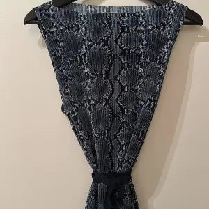 Ursnygg klänning i svart/blå snake skinn mönstring, lite creppat tyg. Hällor hela och band/skärp. Medium men både small o large kan ha den.