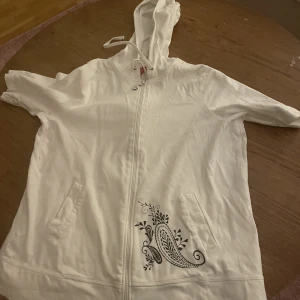Vit kortärmad kofta - Kortärmad vit zip-hoodie! Har ett svart litet mönster vid högra fickan ;)  White Zip-hoodie with short arms! Has a black little pattern near the right pocket:)