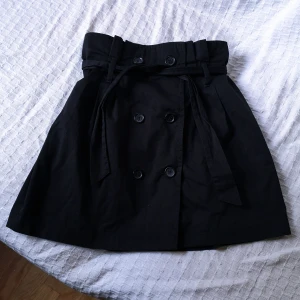 kjol strl s - Kjol som öppnas med knappar, knyts i midjan, skärpet går att ta bort och bytas ut om man vill. Lapparna är bortklippta så vet inte märket eller storlek men skulle säga att den är S. Ca 61cm i midjan och 46cm lång.